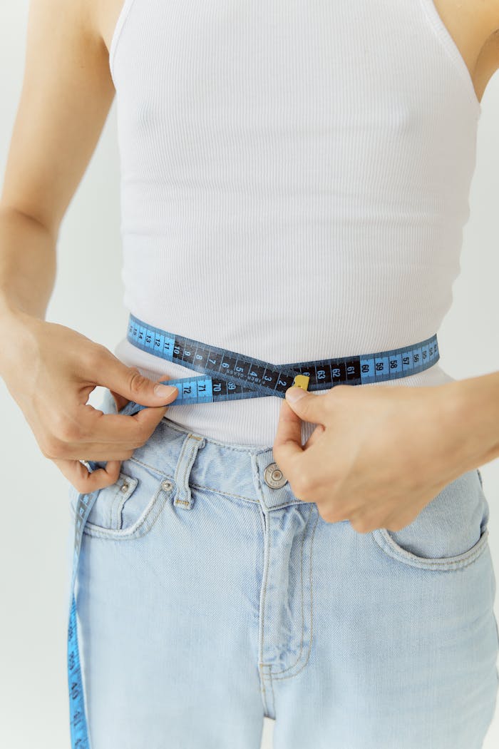 Close-up of a person measuring waist with a blue tape, emphasizing health and fitness.